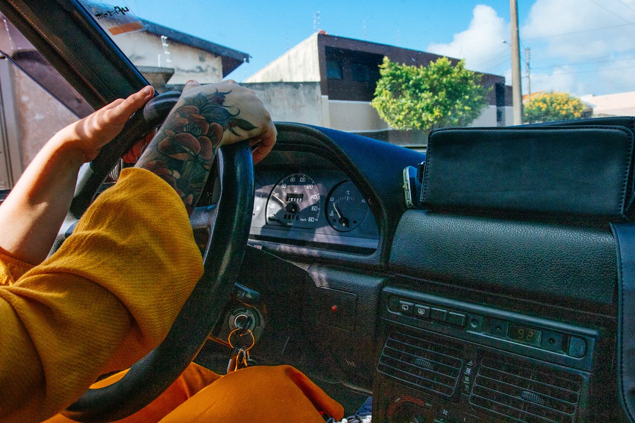 about-bg Close-up of a tattooed person driving a vintage car with a colorful dashboard.