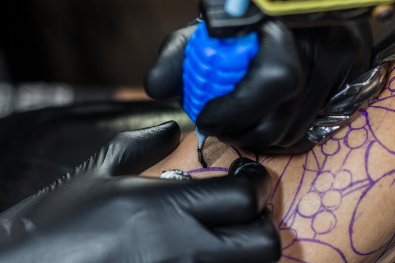 our-story Detailed view of a tattoo artist working on a client's skin using a tattoo machine.
