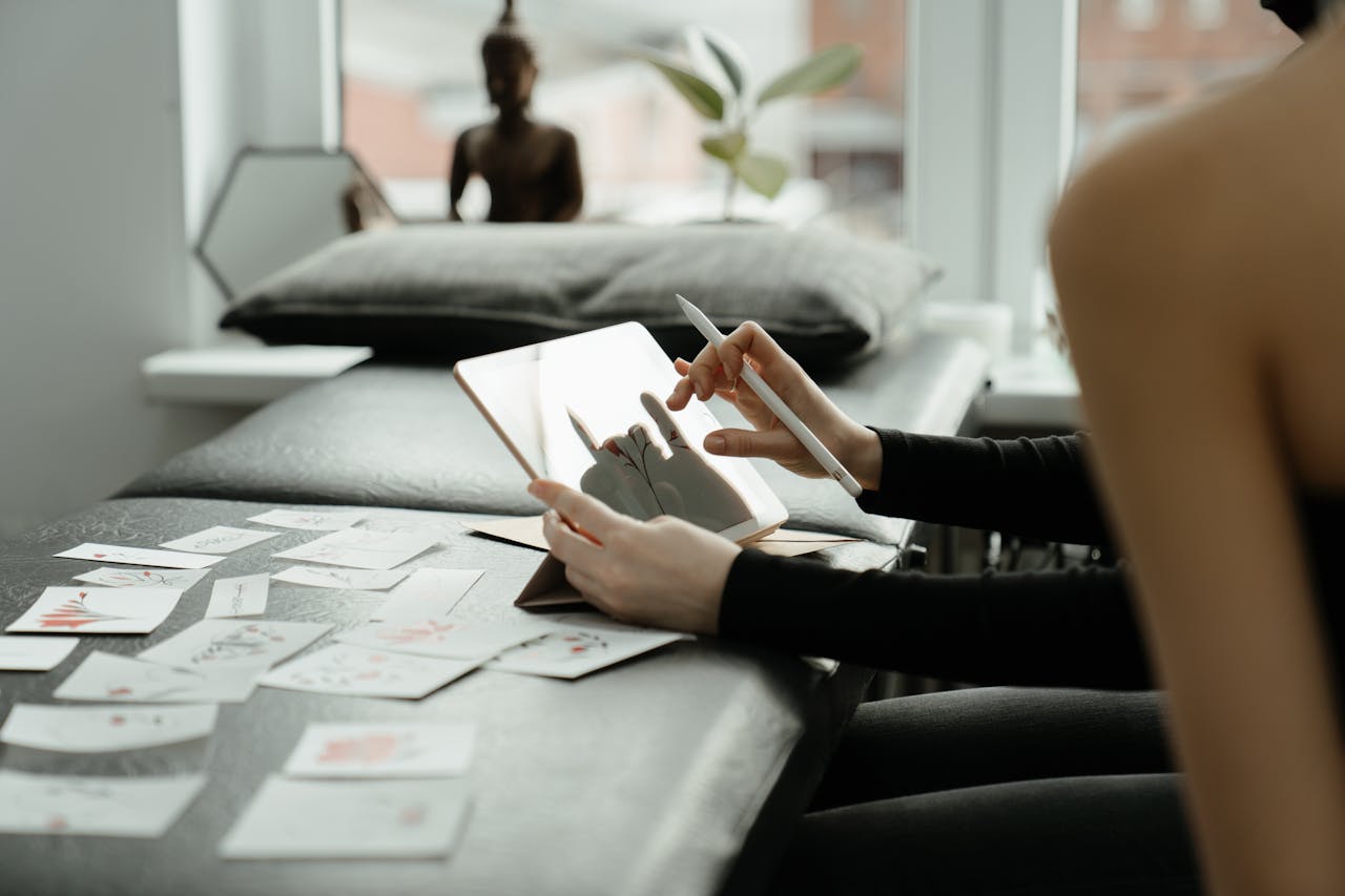 A person sketching tattoo designs on a tablet surrounded by sketches in a studio.